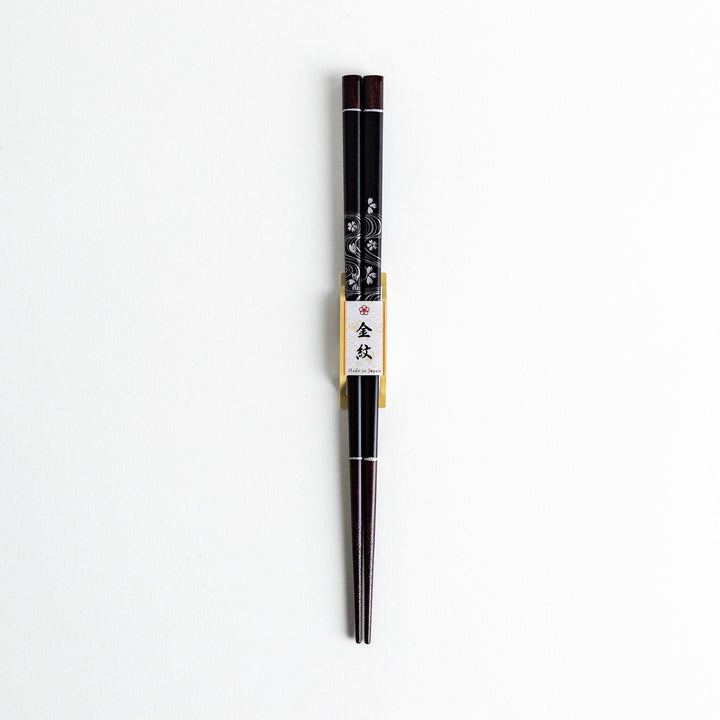 Two pairs of chopsticks, one black and one red, each adorned with intricate floral patterns on a dark background.