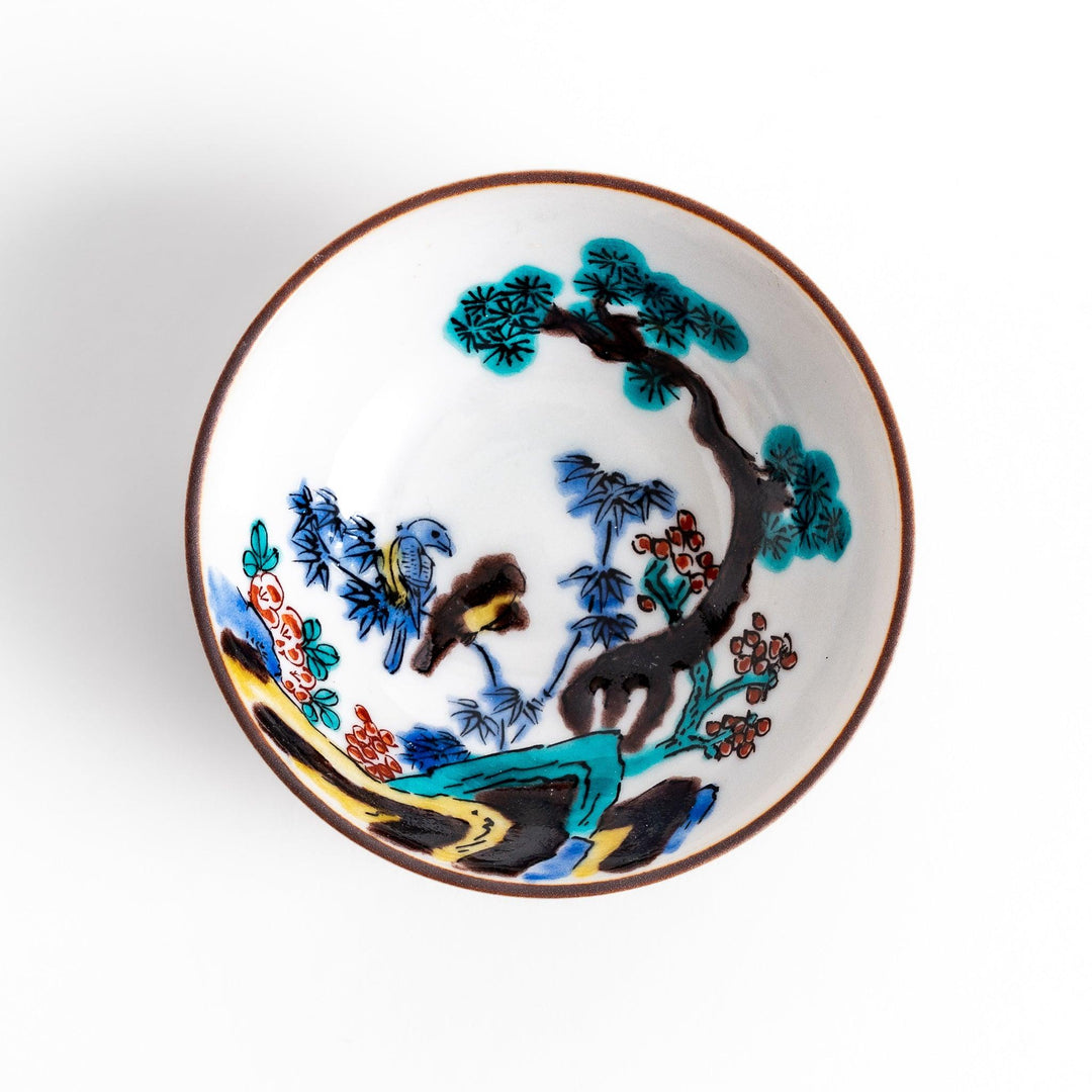 Traditional sake cup showcasing a hand-painted scene of a bird perched on a tree, surrounded by lush greenery, highlighting vibrant colors and Japanese artistry.