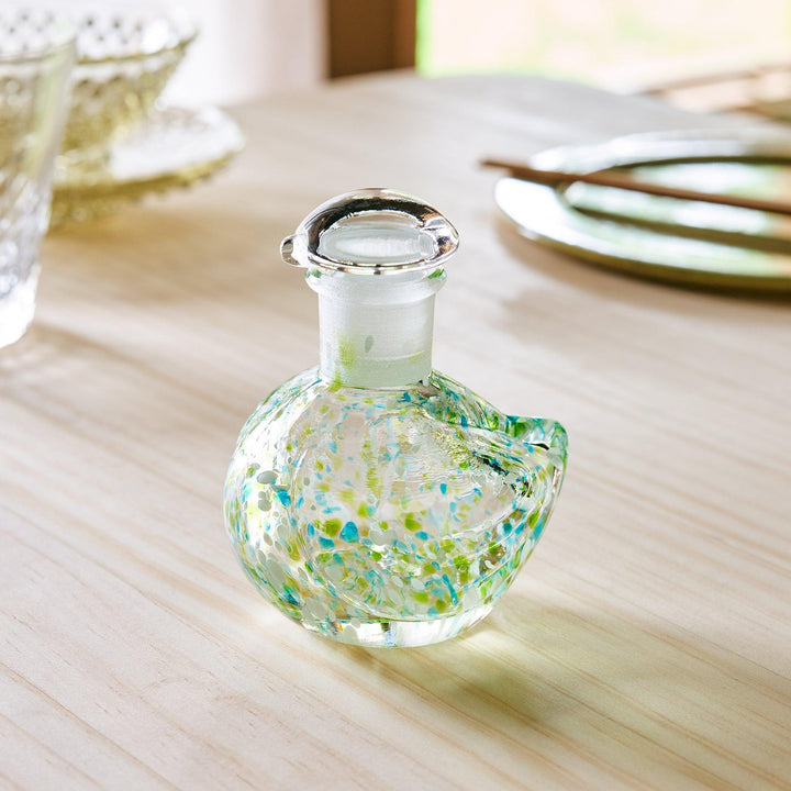 A bird-shaped glass soy sauce dispenser with a frosted stopper, featuring green and blue decorative speckles.
