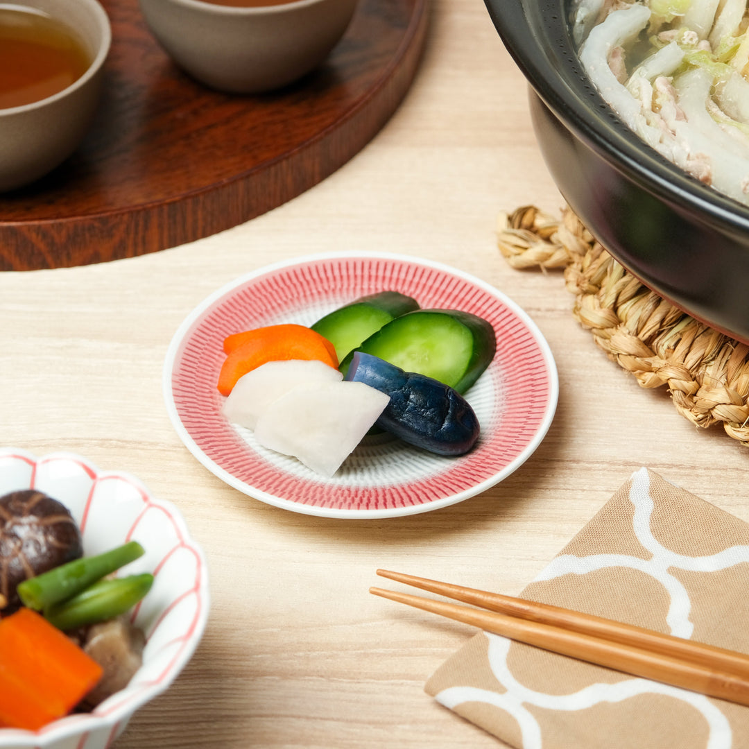 Small Japanese side dish plate with red geometric pattern, holding assorted pickled vegetables including cucumber, carrot, daikon, and eggplant for a traditional meal.