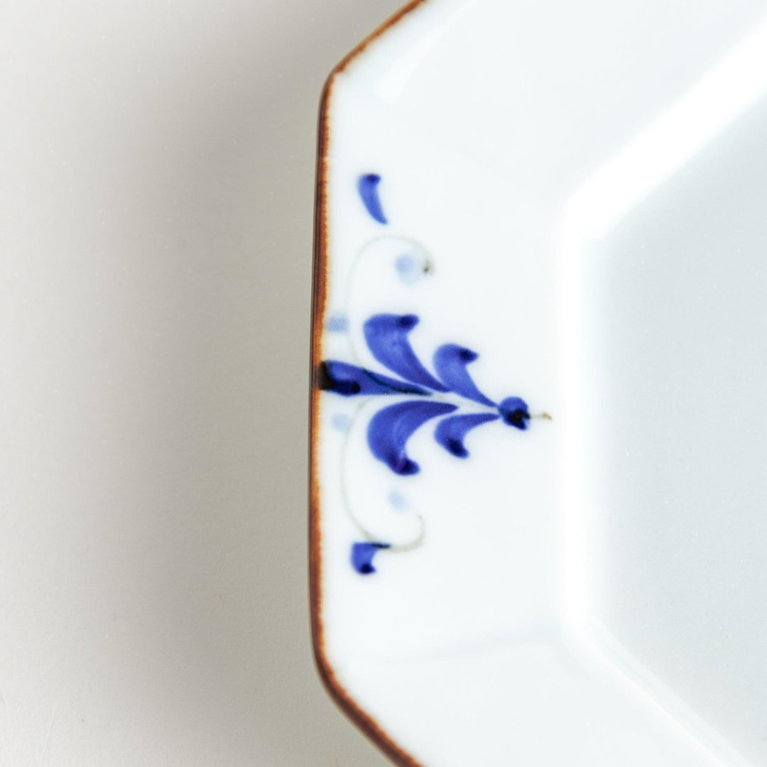 Octagonal white porcelain dessert plate with a blue floral motif and brown accent trim.