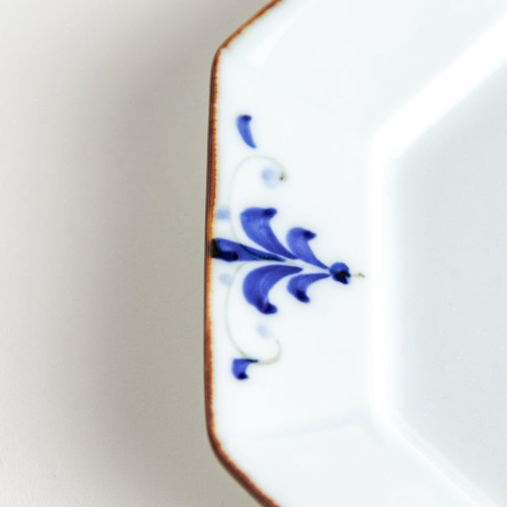 Octagonal white porcelain dessert plate with a blue floral motif and brown accent trim.