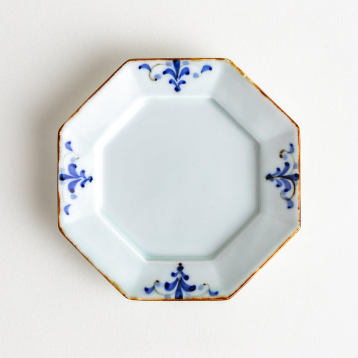 Octagonal white porcelain dessert plate with a blue floral motif and brown accent trim.