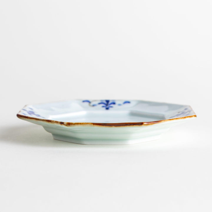 Octagonal white porcelain dessert plate with a blue floral motif and brown accent trim.