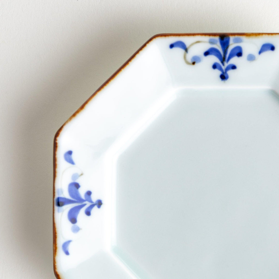 Octagonal white porcelain dessert plate with a blue floral motif and brown accent trim.