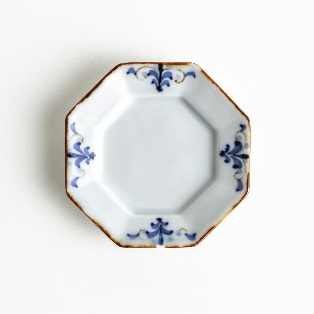 Octagonal white porcelain dessert plate with a blue floral motif and brown accent trim.