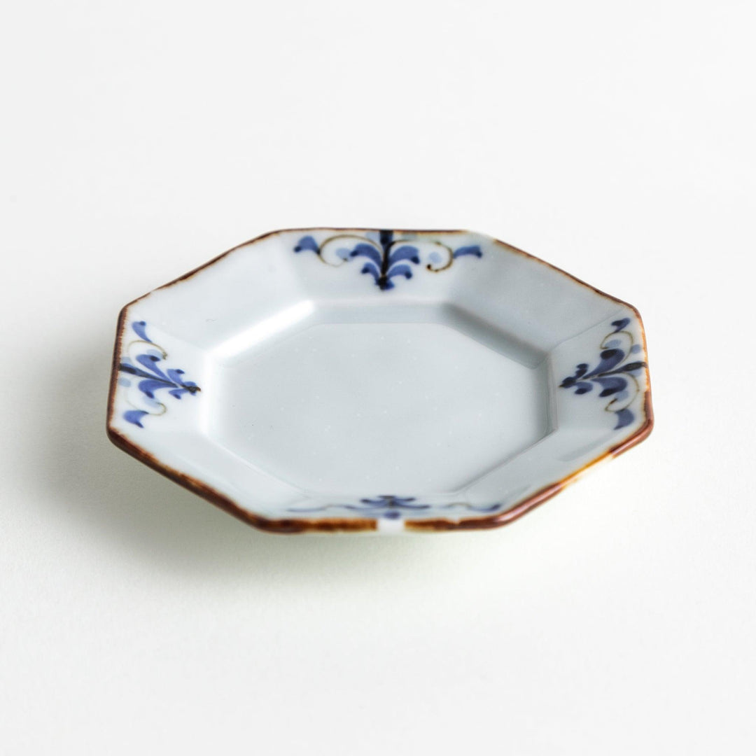 Octagonal white porcelain small sauce dish with a blue floral motif and brown accent trim.
