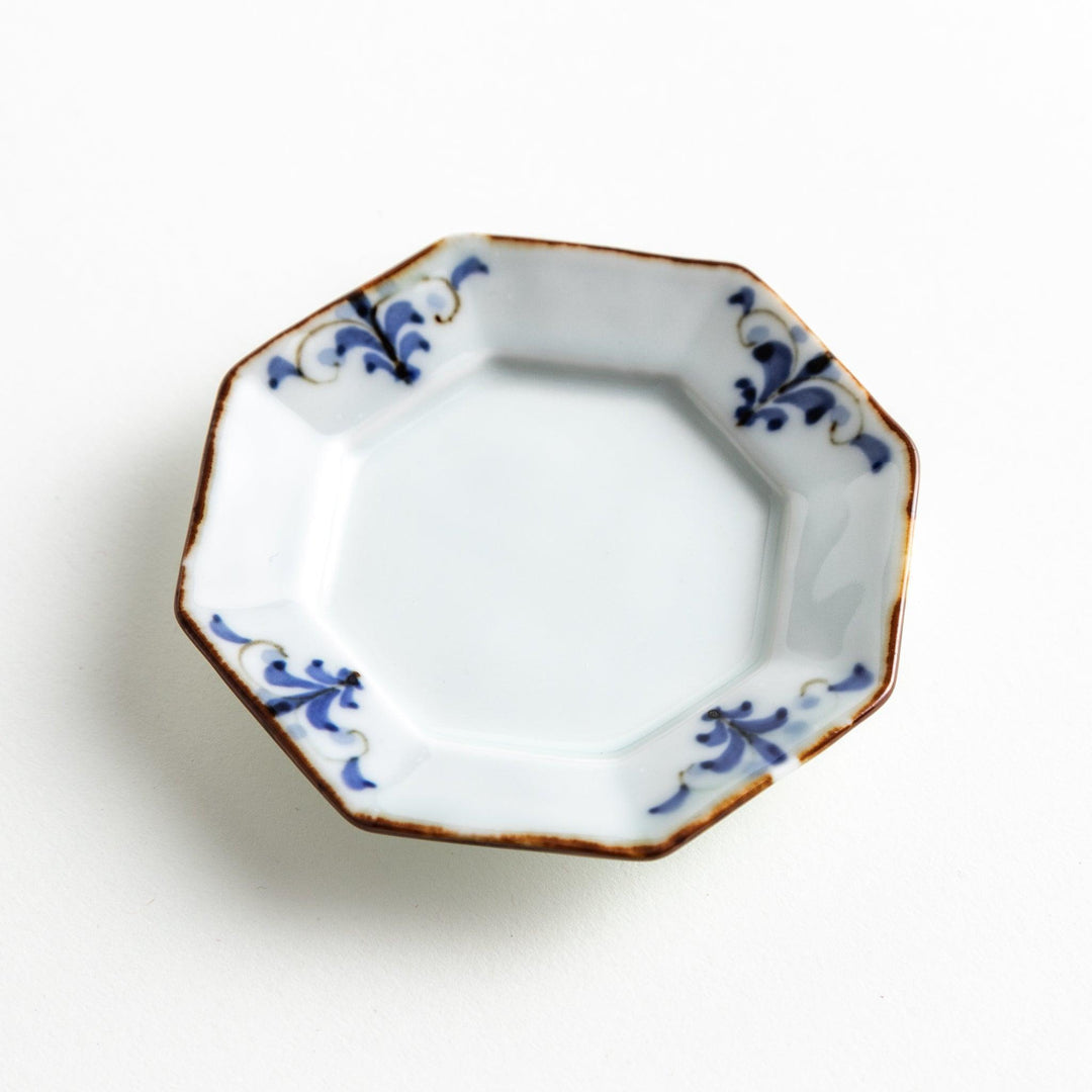 Octagonal white porcelain small sauce dish with a blue floral motif and brown accent trim.