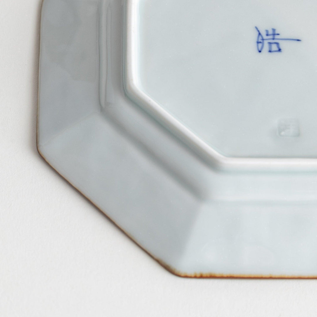 Octagonal white porcelain dessert plate with a blue floral motif and brown accent trim.