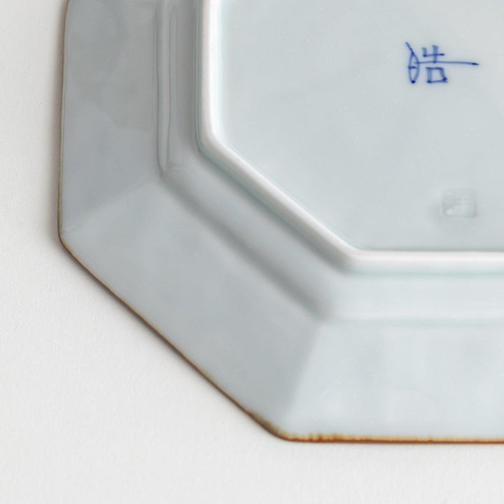 Octagonal white porcelain dessert plate with a blue floral motif and brown accent trim.