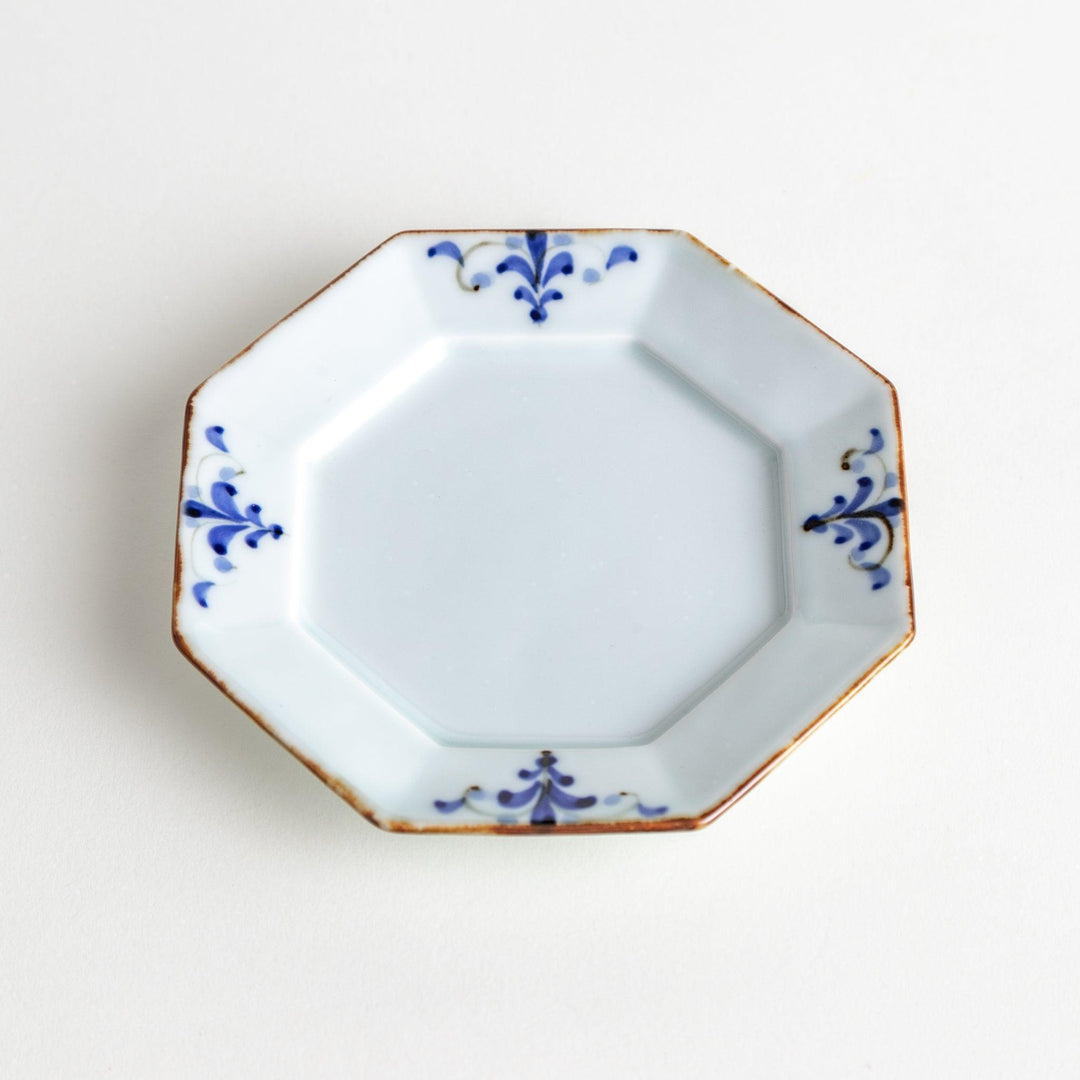 Octagonal white porcelain sauce dish with a blue floral motif and brown accent trim.