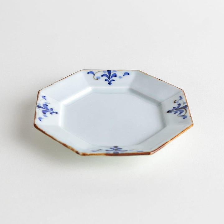 Octagonal white porcelain sauce dish with a blue floral motif and brown accent trim.