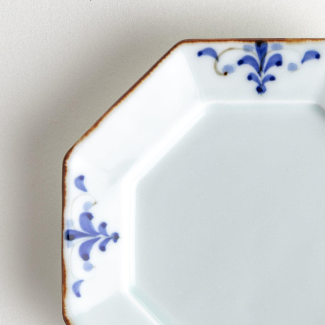 Octagonal white porcelain sauce dish with a blue floral motif and brown accent trim.