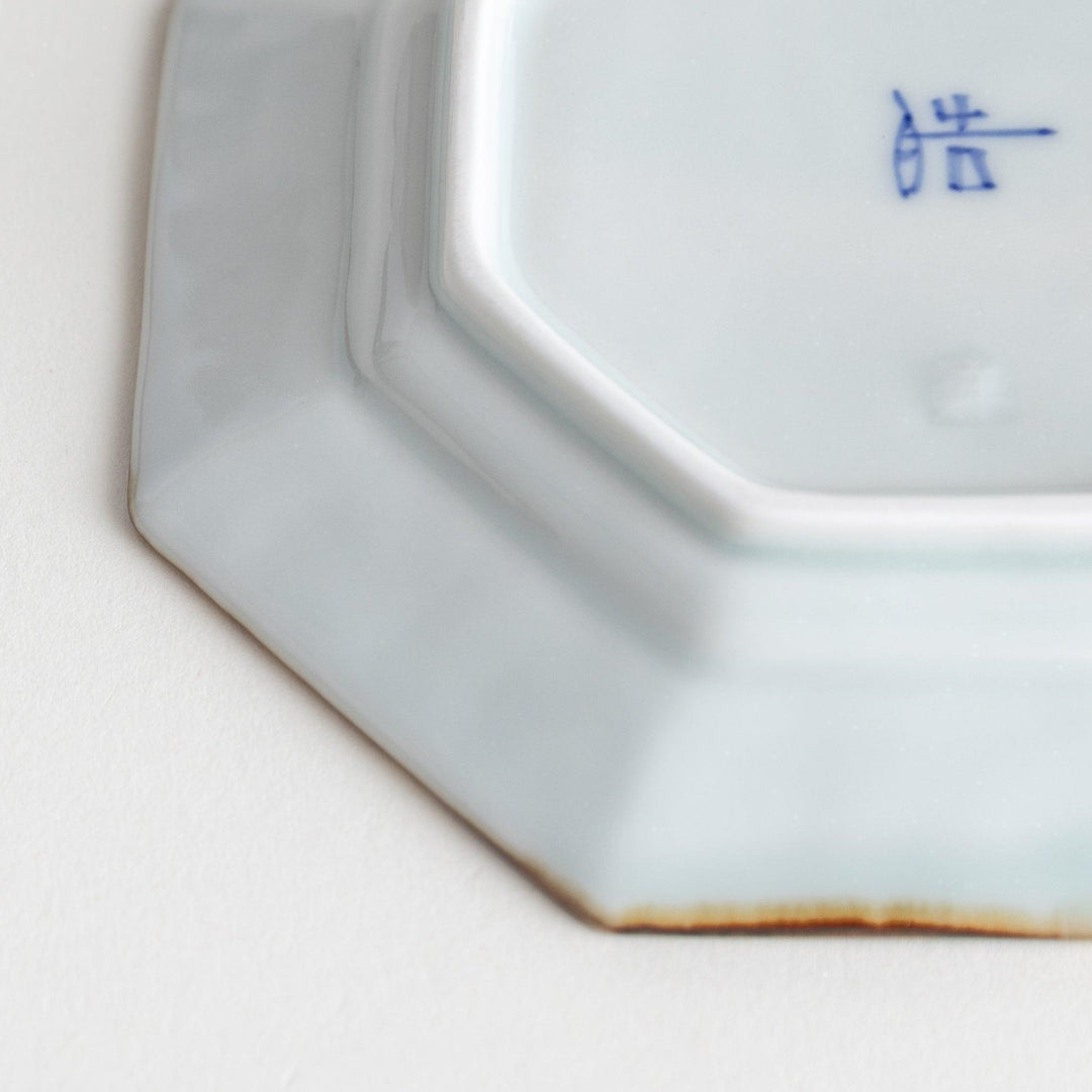 Octagonal white porcelain sauce dish with a blue floral motif and brown accent trim.