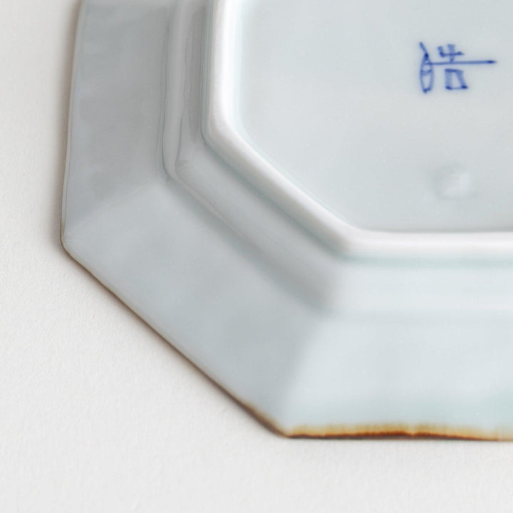 Octagonal white porcelain sauce dish with a blue floral motif and brown accent trim.