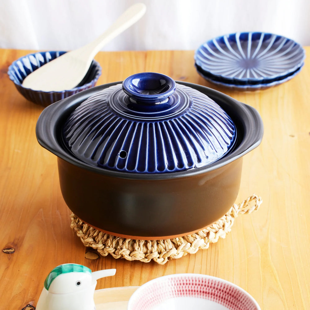 Ginpo Kikka Lapis rice donabe with glossy blue chrysanthemum lid, handcrafted in Japan and placed on dining table for stylish everyday cooking.