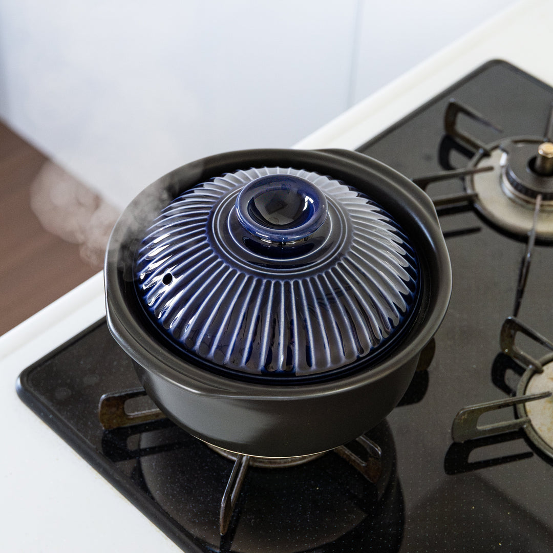 Navy Japanese donabe rice pot with blue lid cooking over gas stove flame