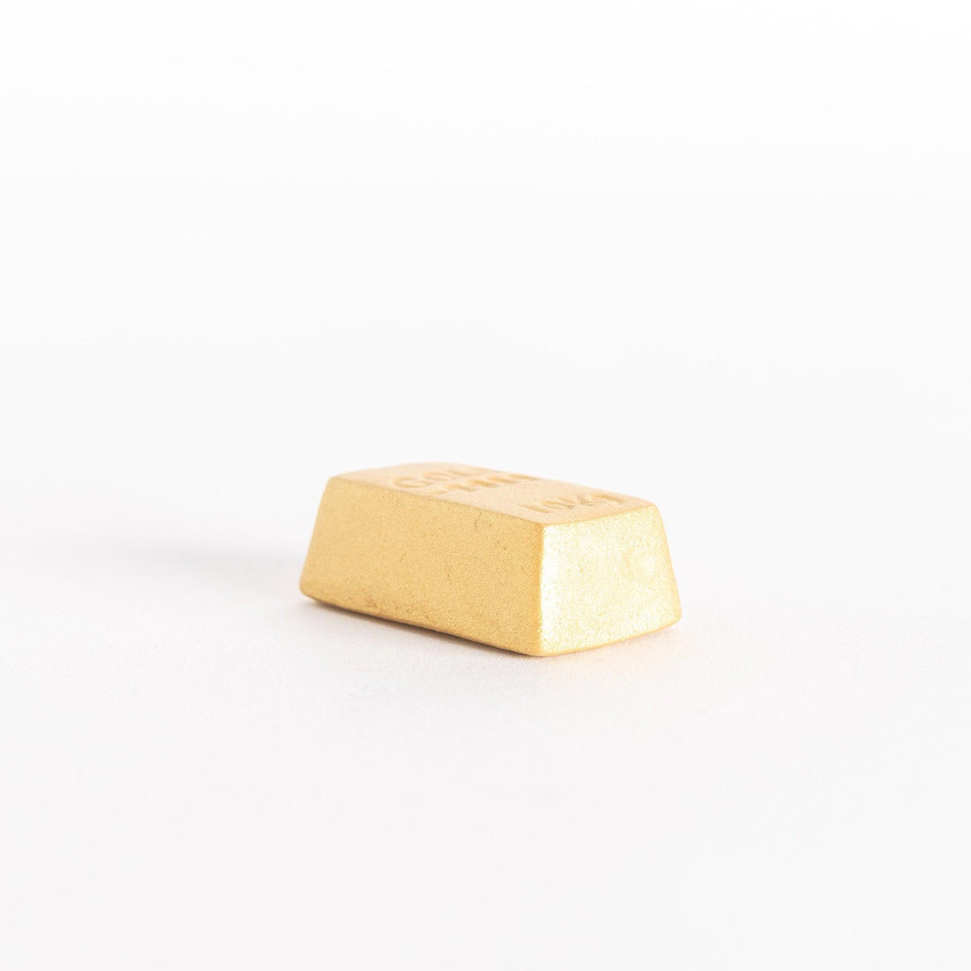 A side-angle view of the gold bar-shaped chopstick rest, highlighting its smooth surface and three-dimensional structure.