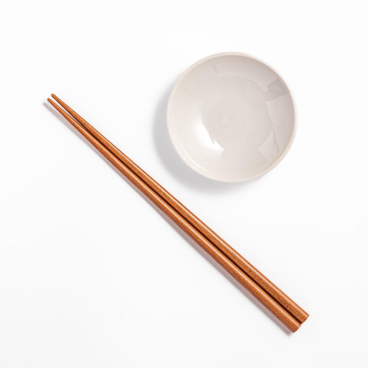 Brown chopsticks and white ceramic dipping dish on hinoki wood sushi plate for elegant sushi presentation