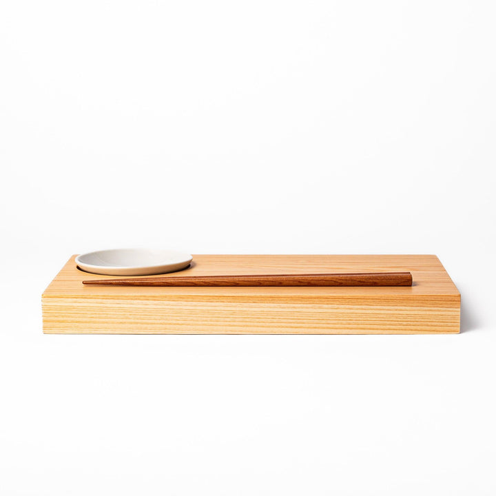 Rectangular hinoki wood sushi plate with brown cooking chopsticks and white ceramic dipping dish for elegant serving.