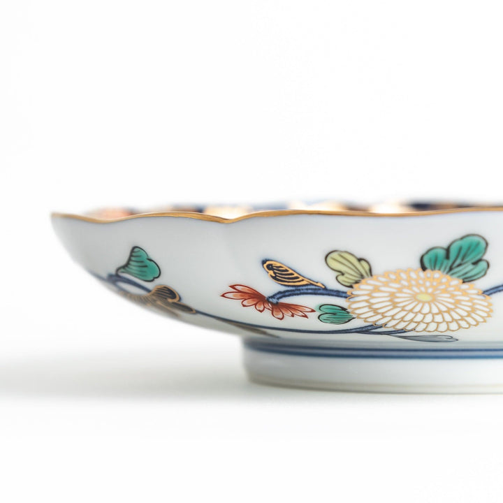 A deep round salad plate with a dark blue background, featuring a central floral design and intricate gold and red patterns with small scenes of Japanese landscapes.