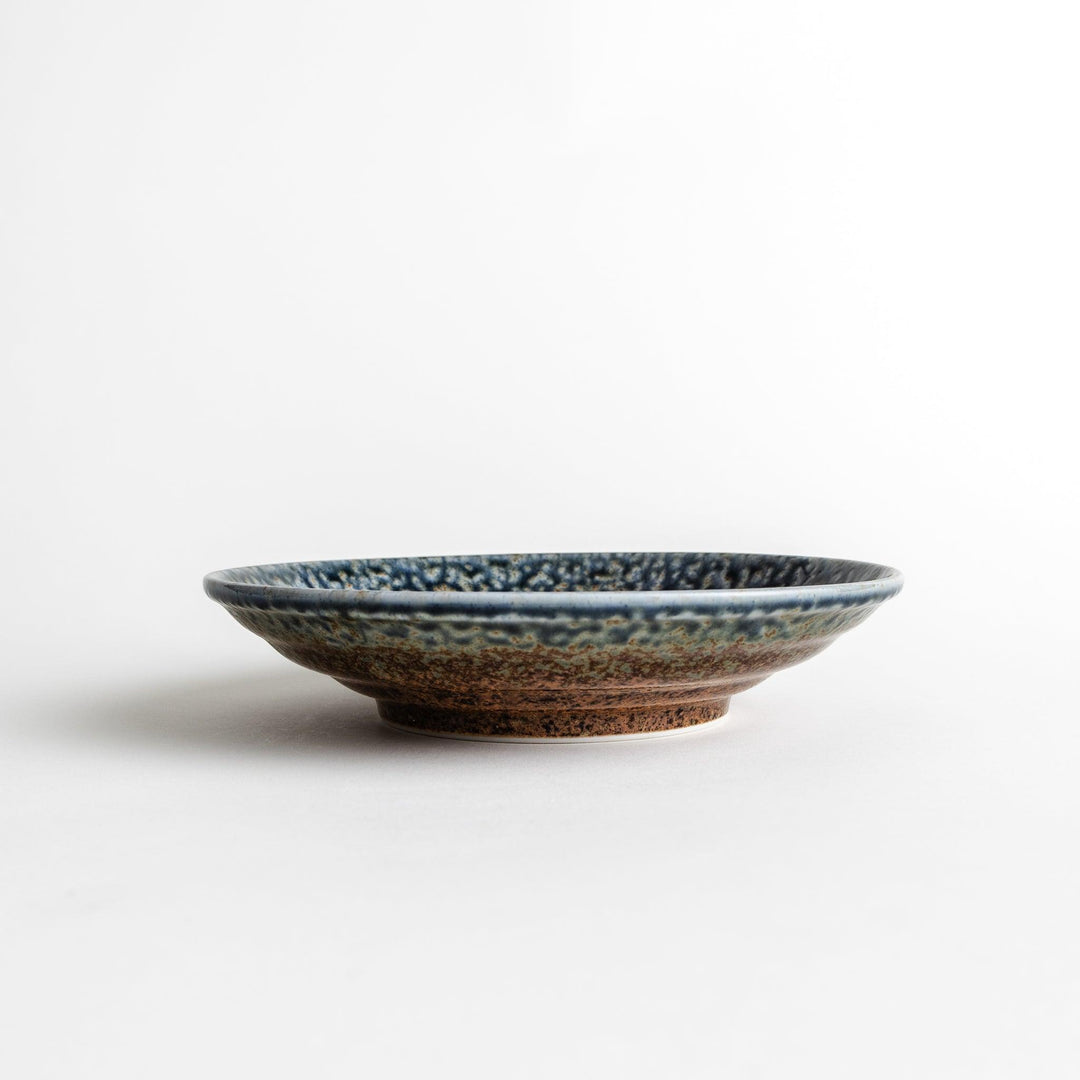 A pasta bowl with a textured glaze in blue, brown, and cream hues, featuring a ridged interior.