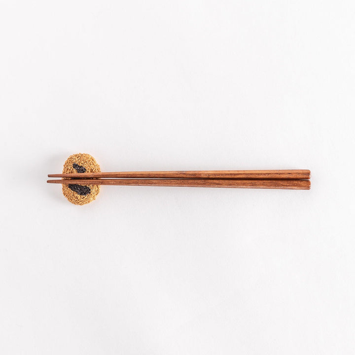 A wider-angle view of a Japanese croquette-shaped chopstick rest with chopsticks placed on top, showing the textured breadcrumb surface and black swirl design.