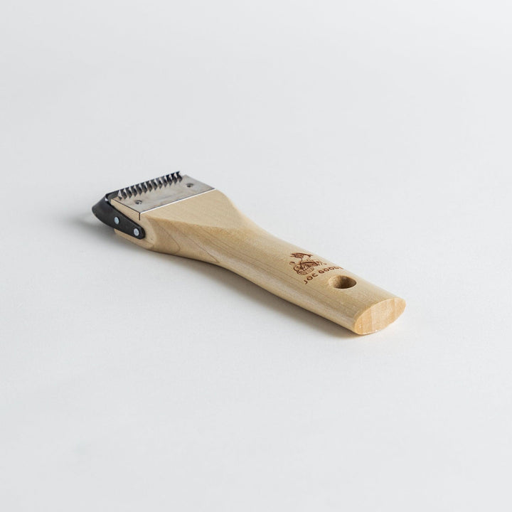 A Wood Handle Julienne Peeler, a piece of kitchenware in use to create thin vegetable strips from a carrot, perfect for salads and garnishes.