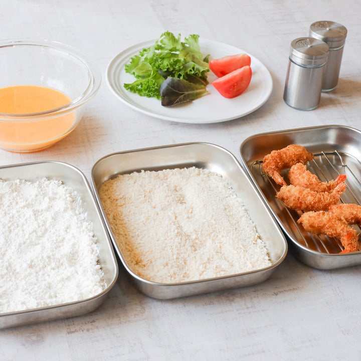 Three stainless steel prep trays used for breading shrimp—flour, panko, and fried pieces—shown alongside egg wash and fresh salad.