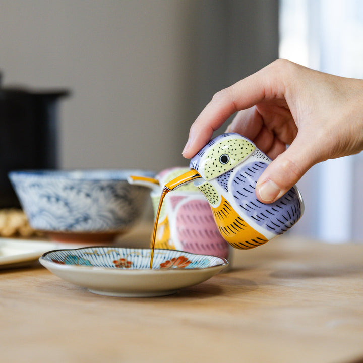 Pouring soy sauce from a purple ceramic kingfisher dispenser into a dipping dish for a gyoza dinner