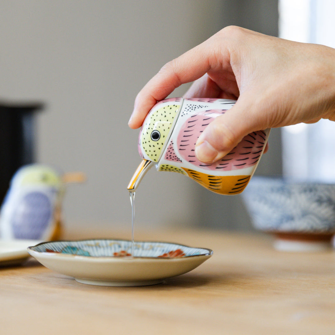 Pouring clear vinegar from a pink ceramic kingfisher soy sauce dispenser into a dish with gyoza background
