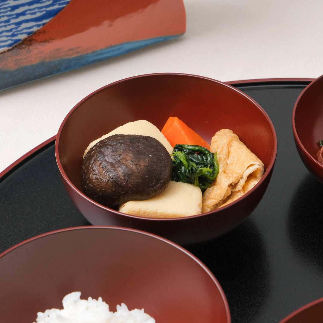 Close-up of Japanese Oryoki bowl filled with simmered vegetables including shiitake mushroom, carrot, tofu, spinach, and fried tofu skin served in a lacquered red bowl.