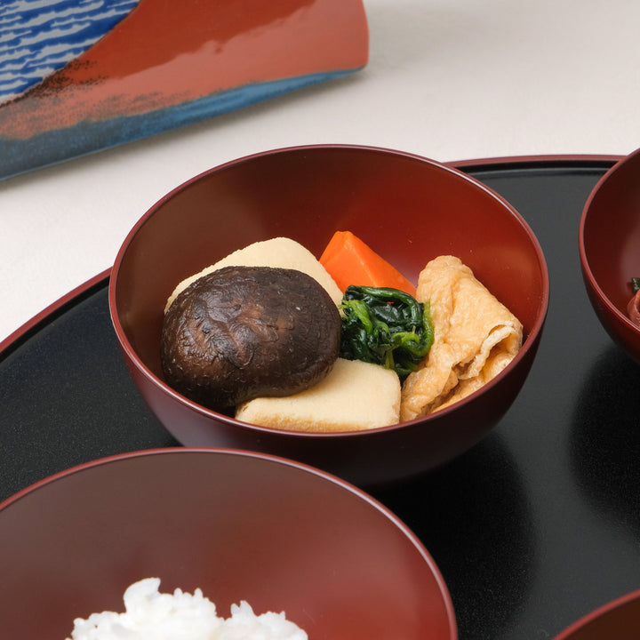 Close-up of Japanese Oryoki bowl filled with simmered vegetables including shiitake mushroom, carrot, tofu, spinach, and fried tofu skin served in a lacquered red bowl.