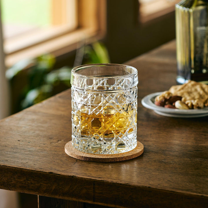 Cut Japanese whiskey glass with a lattice pattern, filled with whisky and ice, placed on a cork coaster.