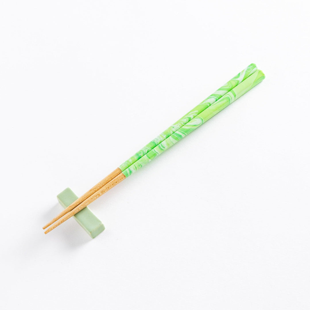 Mint green marbled chopsticks with wooden tips resting on a matching chopstick rest, offering a stylish and functional design.
