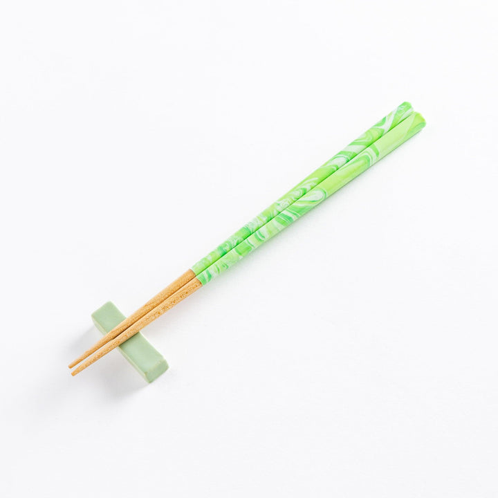 Mint green marbled chopsticks with wooden tips resting on a matching chopstick rest, offering a stylish and functional design.