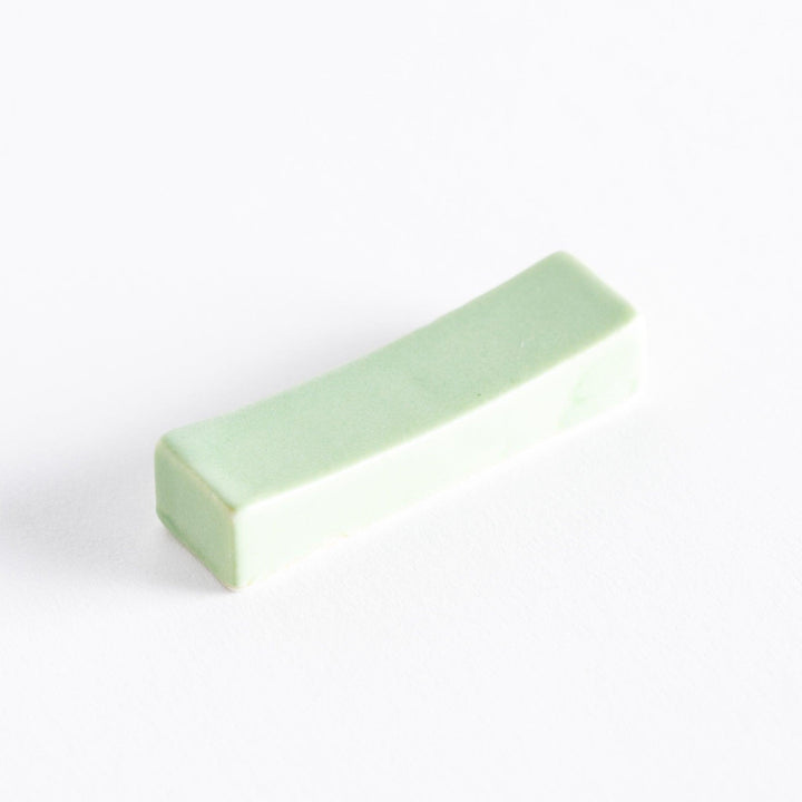 A soft green ceramic chopstick rest, with a smooth and curved surface, adding a delicate touch to your dining table.