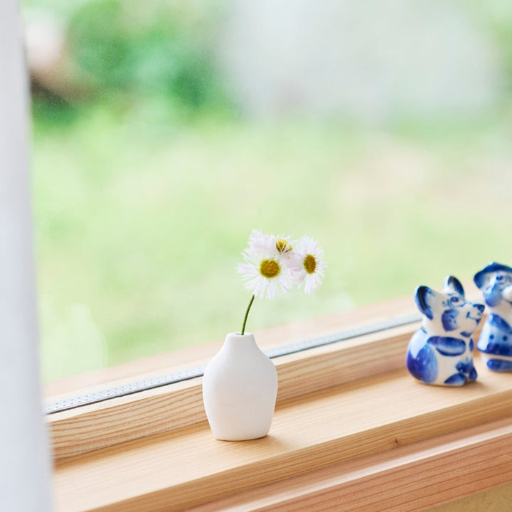 Minimalist white ceramic bud vase with a pear-shaped body and narrow neck, holding two dried flowers for a soft, elegant decorative touch.