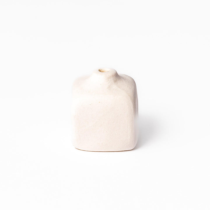 Minimalist white ceramic bud vase with a rounded square shape and narrow opening, perfect for adding subtle elegance to small floral arrangements.