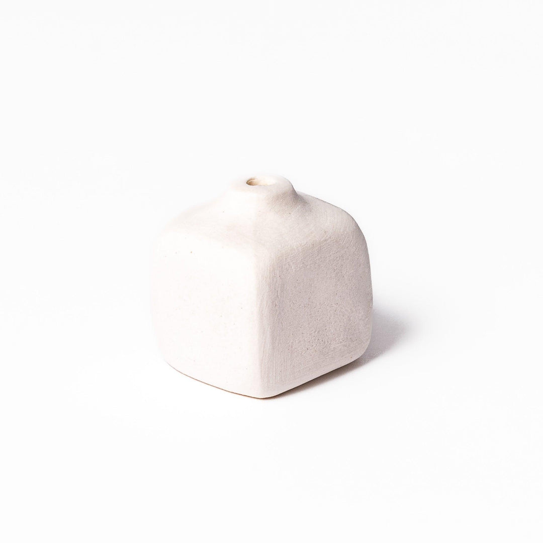 Minimalist white ceramic bud vase with a rounded square shape and narrow opening, perfect for adding subtle elegance to small floral arrangements.