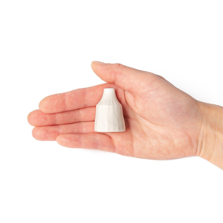 Minimalist white ceramic bud vase with a faceted prism shape and narrow neck, offering a modern geometric touch for single stems or dried flowers.