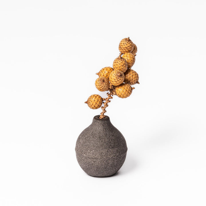 Minimalist dark ceramic bud vase with a rounded orb shape and narrow opening, perfect for displaying a single stem with a rustic, earthy charm.