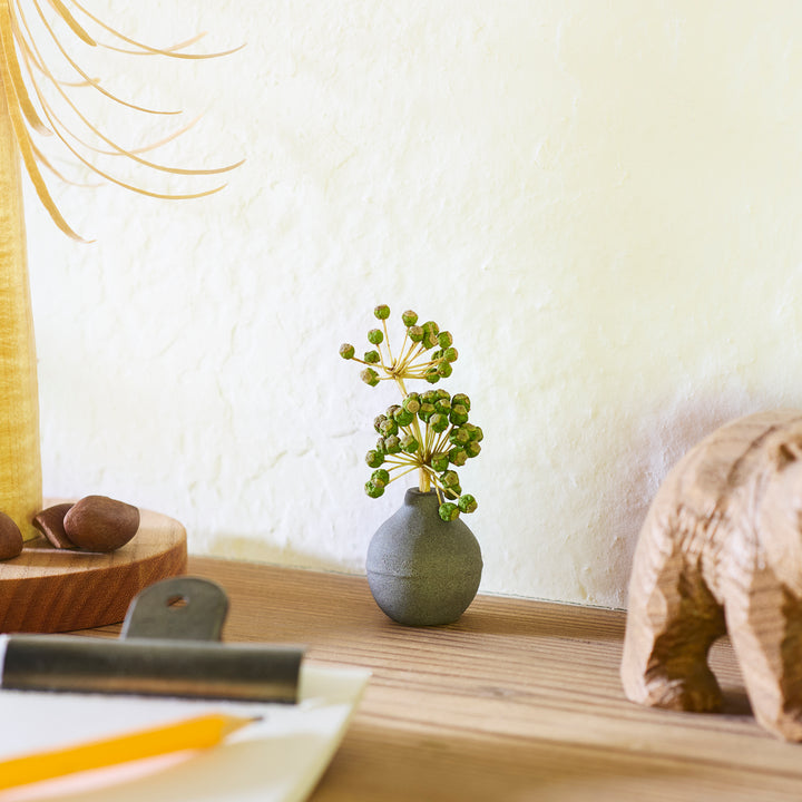 Minimalist dark ceramic bud vase with a rounded orb shape and narrow opening, perfect for displaying a single stem with a rustic, earthy charm.