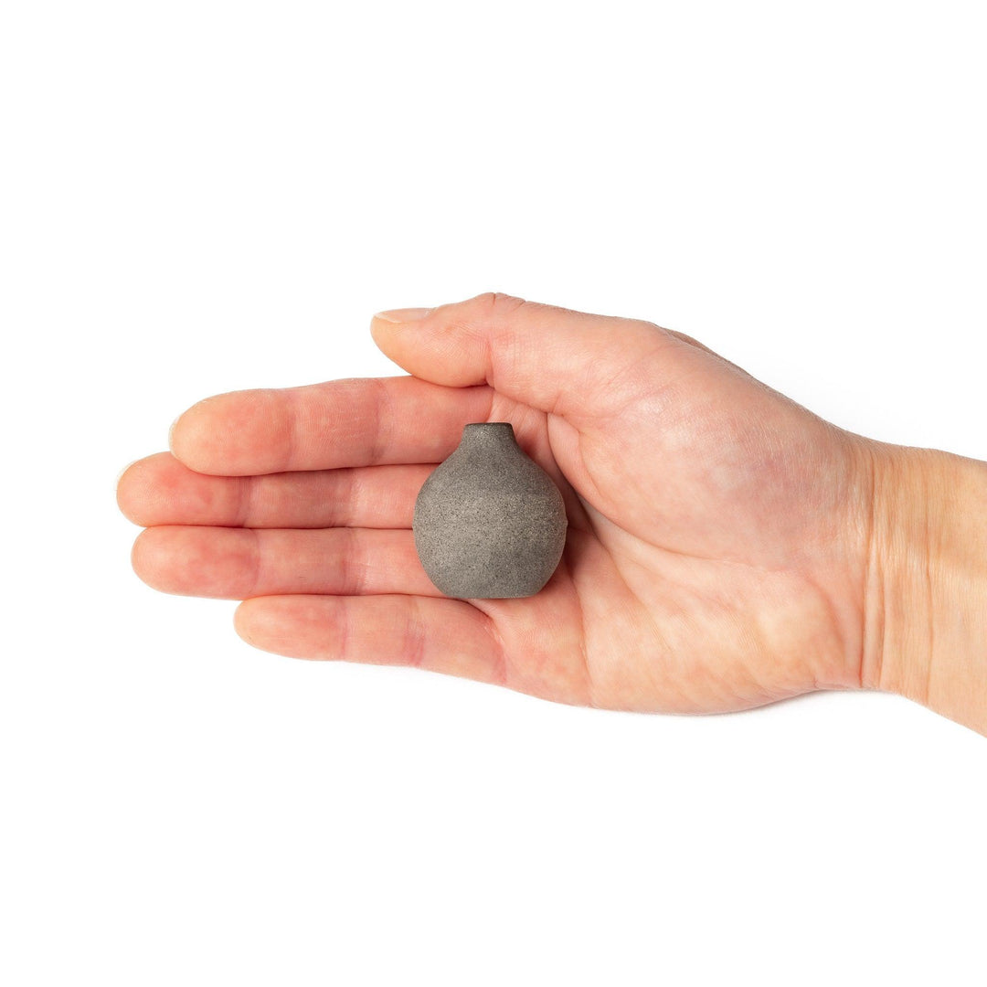 Minimalist dark ceramic bud vase with a rounded orb shape and narrow opening, perfect for displaying a single stem with a rustic, earthy charm.