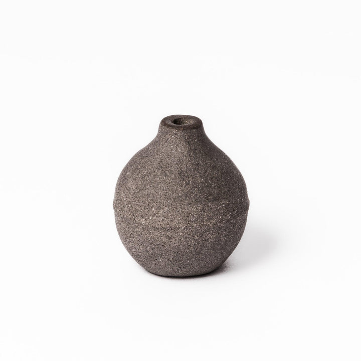 Minimalist dark ceramic bud vase with a rounded orb shape and narrow opening, perfect for displaying a single stem with a rustic, earthy charm.