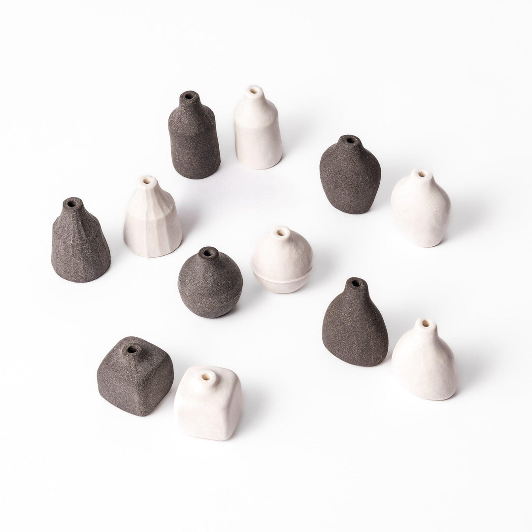 A full set of minimalist ceramic bud vases in soft white and dark finishes, showcasing various forms including teardrop, pear, prism, orb, square, and cylinder. Perfect for displaying single stems or small arrangements with a modern, earthy aesthetic.