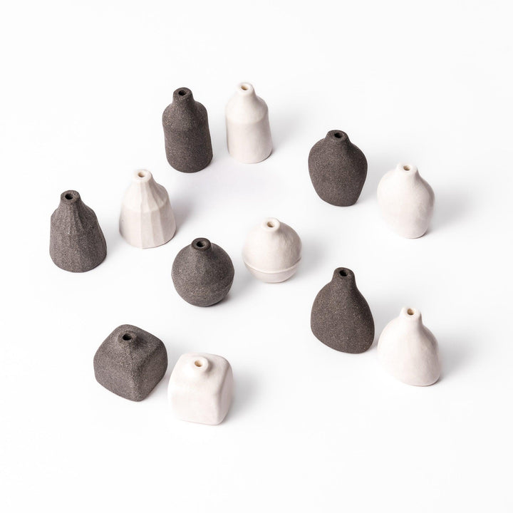 A full set of minimalist ceramic bud vases in soft white and dark finishes, showcasing various forms including teardrop, pear, prism, orb, square, and cylinder. Perfect for displaying single stems or small arrangements with a modern, earthy aesthetic.