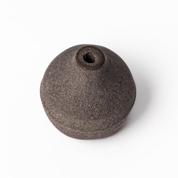 Minimalist dark ceramic bud vase with a rounded orb shape and narrow opening, perfect for displaying a single stem with a rustic, earthy charm.