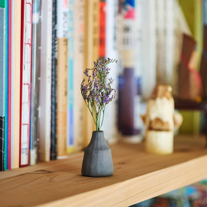 Minimalist dark ceramic bud vase with a faceted prism-like form and matte texture, ideal for adding a sculptural touch to small arrangements.