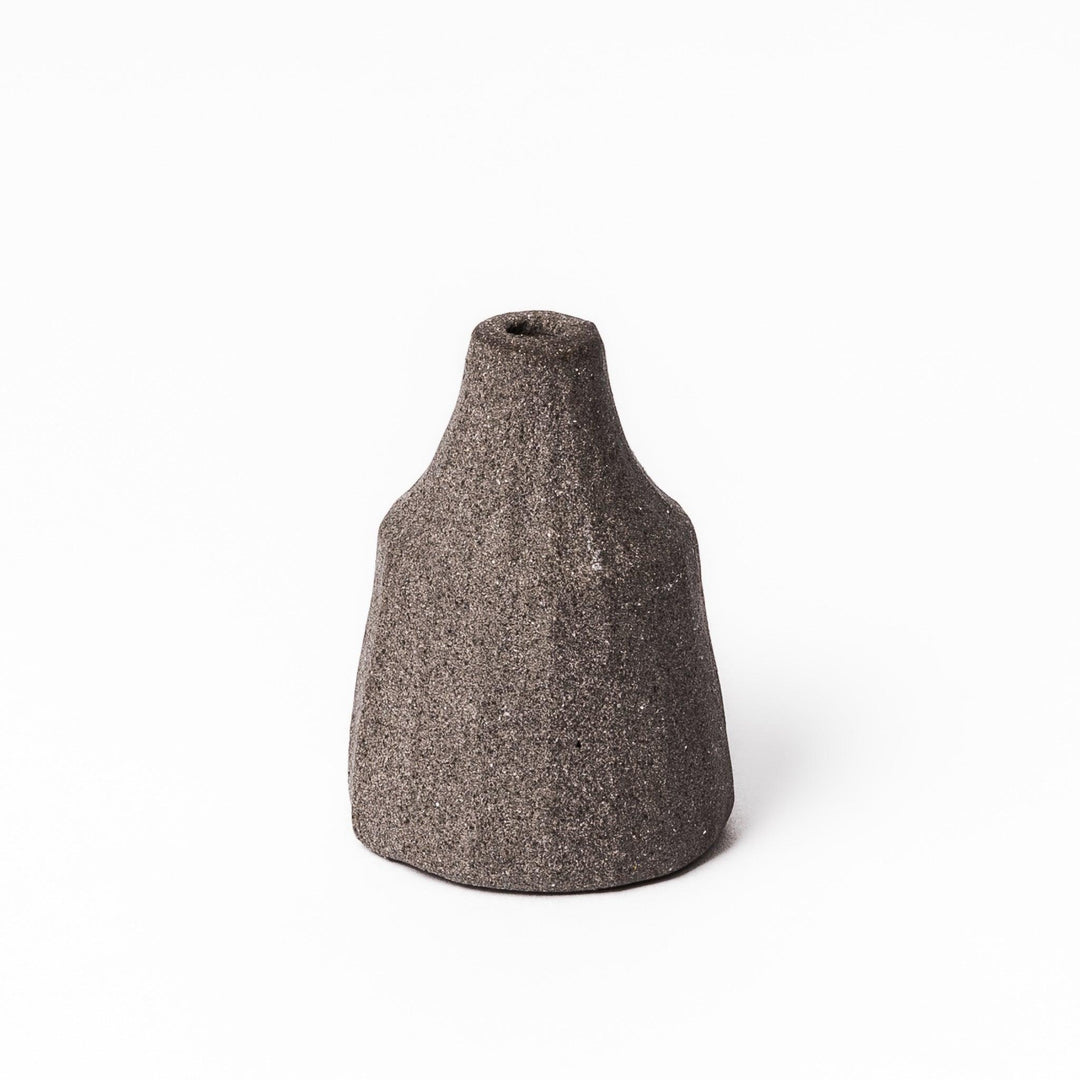 Minimalist dark ceramic bud vase with a faceted prism-like form and matte texture, ideal for adding a sculptural touch to small arrangements.
